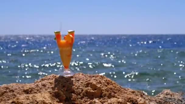 Succo di frutta fresca tropicale in un bicchiere con paglia sulla spiaggia d'Egitto sta su una roccia vicino al mare — Video Stock