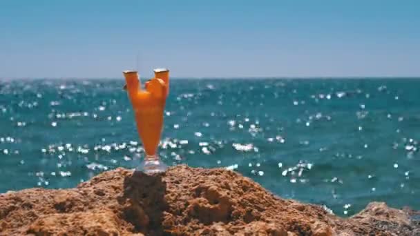 エジプトのビーチでストローとガラスのトロピカルフレッシュカクテルは、紅海の背景に岩の上に立っています — ストック動画