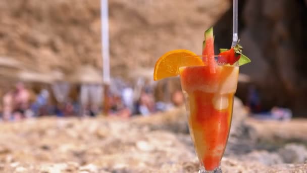 Тропический свежий коктейль в стакане с соломой на пляже Египта стоит на скале на фоне Красного моря — стоковое видео