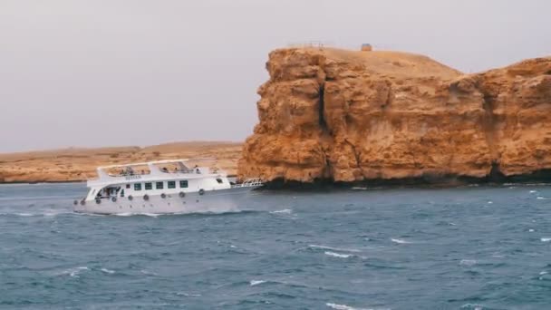 Piacere barca con le vele turistiche nel mare in tempesta sullo sfondo di rocce. Egitto — Video Stock