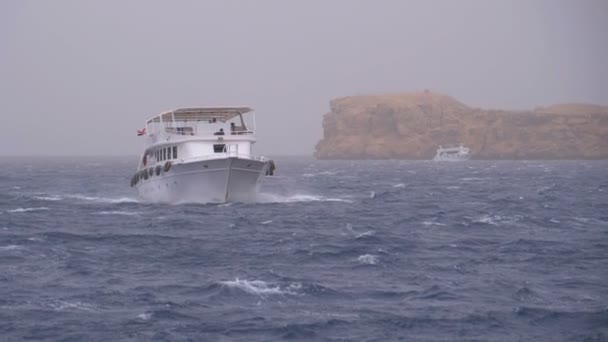 Лодка удовольствия с туристами плавает в бурном море на фоне скал. Египет — стоковое видео