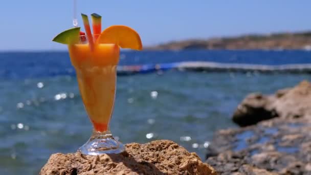 Tropische frischen Cocktail in einem Glas mit Stroh am Strand von Ägypten steht auf einem Felsen vor dem Hintergrund des roten Meeres — Stockvideo
