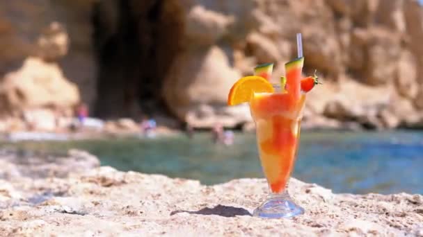 Tropischen frischen Saft in einem Glas mit Stroh am Strand von Ägypten steht auf einem Felsen am Meer — Stockvideo