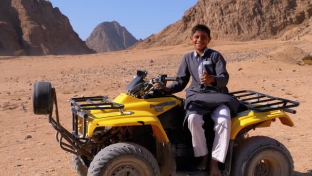 Arabian Kid se sienta en Quad Bike off-road en el fondo del desierto y las montañas en Egipto — Vídeo de stock