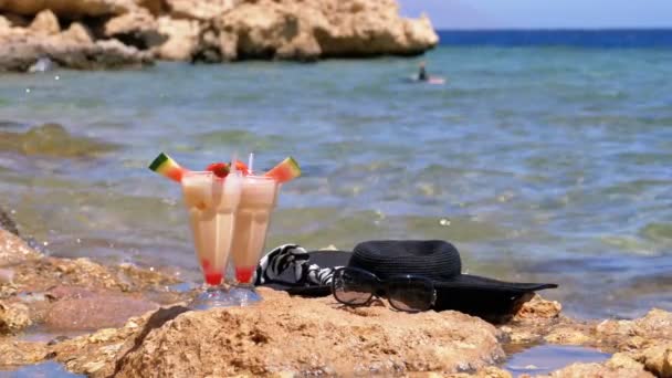 エジプトのビーチでストローとガラスのトロピカルフレッシュジュースは、海辺の岩の上に立っています。スローモーション — ストック動画