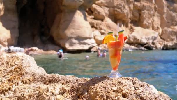 在埃及海滩上的玻璃杯中用稻草的热带新鲜鸡尾酒站在红海背景的岩石上 — 图库视频影像