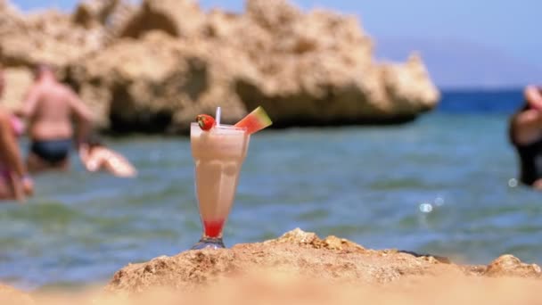 Tropisk färsk juice i ett glas med halm på stranden i Egypten står på en klippa vid havet. Slow motion — Stockvideo