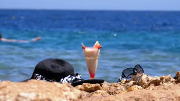 Succo di frutta fresca tropicale, cappello e bicchieri sulla spiaggia d'Egitto sta su una roccia vicino al Mar Rosso — Video Stock