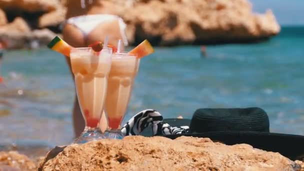 エジプトのビーチで熱帯フレッシュジュース、帽子、メガネが紅海の岩の上に立つ — ストック動画