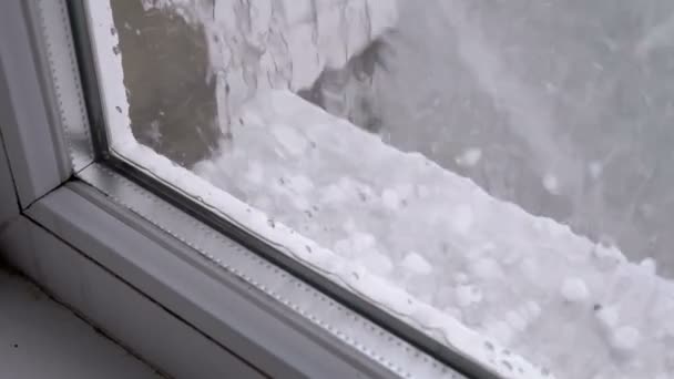 Hagel buiten het raam. Stukjes hagel vallen op de vensterbank achter een plastic raam — Stockvideo
