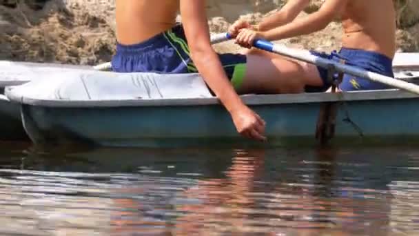 De jongens in de oude boot zweven op de rivier en roeien roeiriemen. — Stockvideo