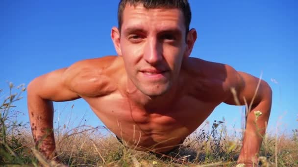 Young Athletic man med en naken torso utför push-ups med klappar på naturen. Slow motion — Stockvideo