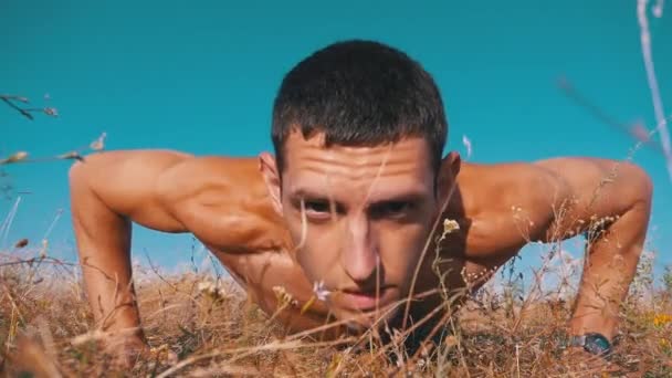 Jovem atlético com um tronco nu realiza flexões sobre a natureza. Movimento lento — Vídeo de Stock