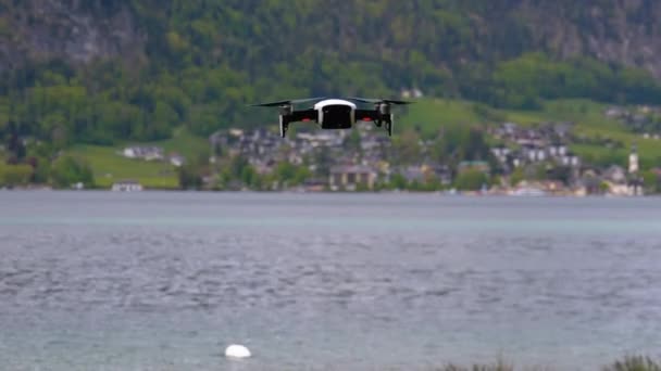 Drone met roterende propellers hangend in de lucht op een achtergrond van meer en bergen — Stockvideo