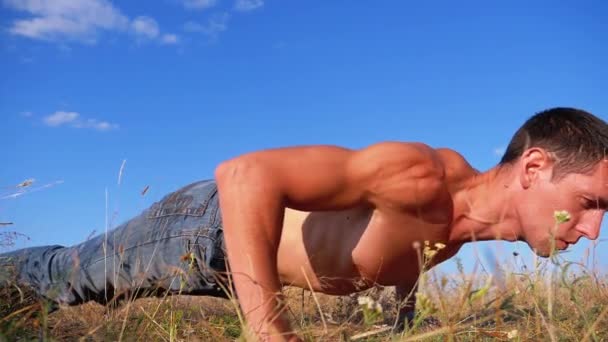 Νέος αθλητικός άνθρωπος με ένα γυμνό κορμό εκτελεί κάμψεις στη φύση. Αργή κίνηση — Αρχείο Βίντεο