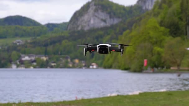 Dron s rotujícími vrtulemi visícími ve vzduchu na pozadí jezera a hor — Stock video