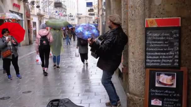 Street musiker spelar gitarr på den berömda gatan i gamla stan i Salzburg i regn. Österrike — Stockvideo
