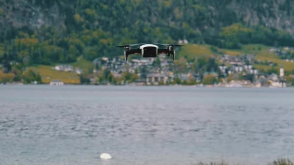 Drone con hélices giratorias colgando en el aire sobre un fondo de lago y montañas — Vídeos de Stock