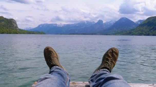 Ludzkie nogi na tle górskiego jeziora i pokrytych śniegiem gór. — Wideo stockowe