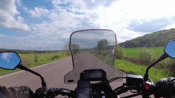 グリーンフィールズとヒルズの近くの美しい空の道に乗ってモーターサイクリスト。一人称ビュー — ストック動画