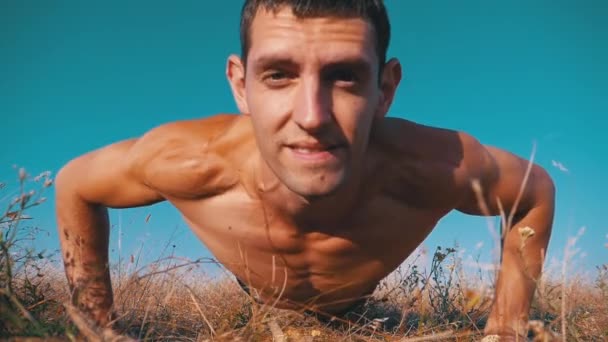 Hombre atlético joven con un torso desnudo realiza flexiones con aplausos en la naturaleza. Moción lenta — Vídeo de stock