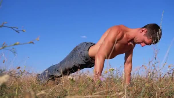 Ung atletisk man med en naken torso utför armhävningar på naturen — Stockvideo