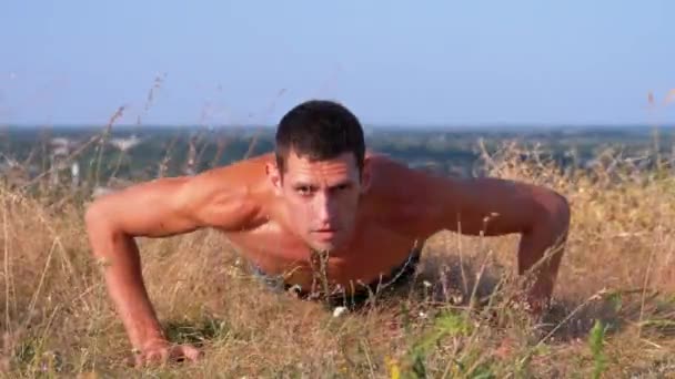 Hombre atlético joven con un torso desnudo realiza flexiones en la naturaleza — Vídeos de Stock