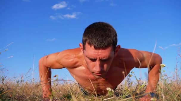 Hombre atlético joven con un torso desnudo realiza flexiones con aplausos en la naturaleza. Moción lenta — Vídeos de Stock