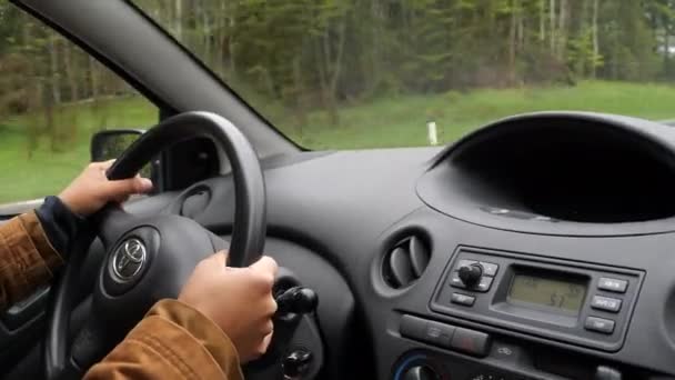Женщина водит машину в дождливую погоду. Женские руки на руле автомобиля во время движения — стоковое видео