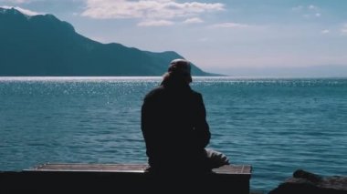 Bir Göl ve Dağların arka planında bir Bankta Oturan Yalnız Yaşlı Bir Adamın Silueti