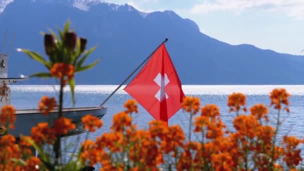 Schweizer Flagge vor dem Hintergrund alpiner Berge und Blumen in der Nähe des Genfersees — Stockvideo
