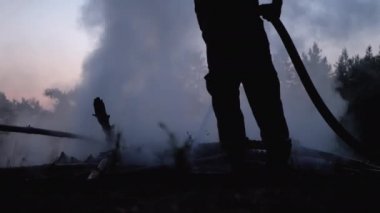 Firehose tarafından Su ile Yangın söndürmek. İtfaiyeci hortum tutun ve akşam orman kamp ateşi söndürmek