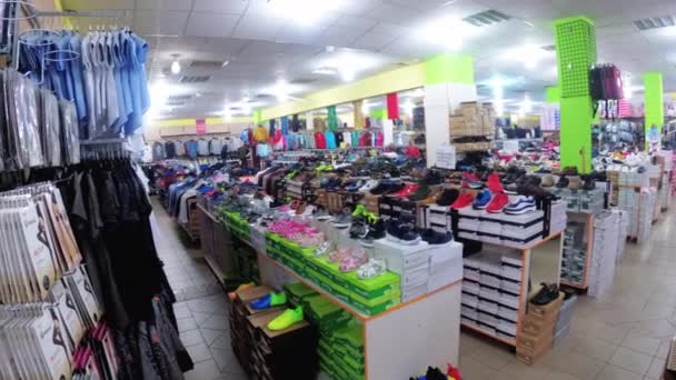 Ropa se encuentra en bastidores y cuelga en perchas en una tienda de ropa . — Vídeos de Stock