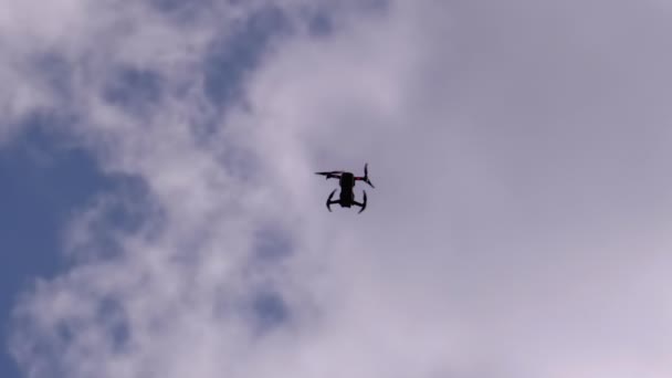 Silueta de un dron sobre un fondo de cielo azul con nubes que vuelan en el aire — Vídeos de Stock