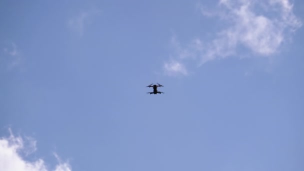 Silhueta de um drone em um fundo de céu azul com nuvens que voa no ar — Vídeo de Stock