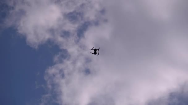 Silhueta de um drone em um fundo de céu azul com nuvens que voa no ar — Vídeo de Stock