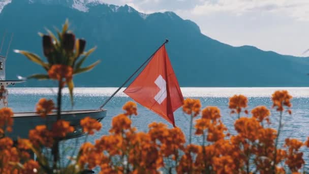 Schweizisk flagga på en bakgrund av alpina berg och blommor nära Genèvesjön — Stockvideo