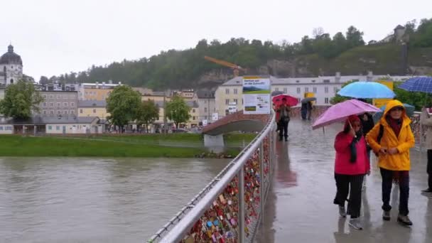 Ludzie z parasolami spacer na most miłości w Salzburgu podczas deszczu, Austria. — Wideo stockowe