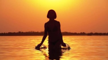 Gün batımında Kadın Siluet Ilerler Eller yükseltir ve Su Sıçramaları Oluşturma. Yavaş çekim