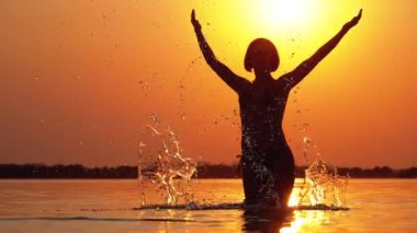 Gün batımında Kadın Siluet Ilerler Eller yükseltir ve Su Sıçramaları Oluşturma. Yavaş çekim