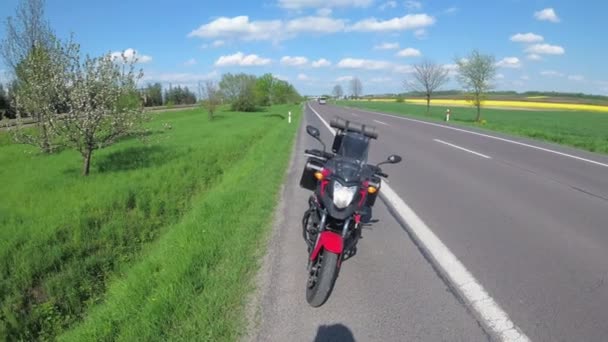 Motocykl stoi po stronie pustej drogi w słoneczny dzień. — Wideo stockowe