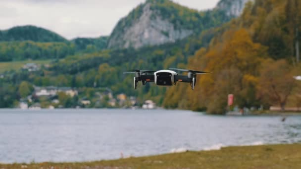 Drohne mit rotierenden Propellern hängt in der Luft vor dem Hintergrund von See und Bergen — Stockvideo