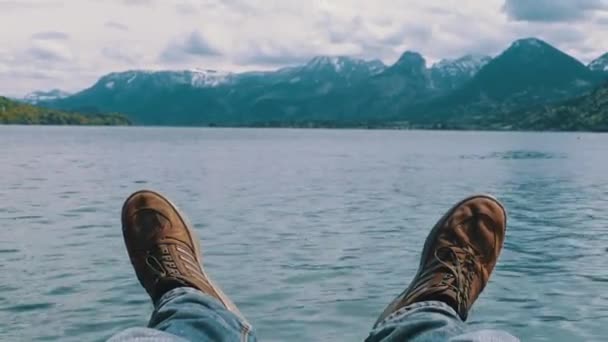 Ludzkie nogi na tle górskiego jeziora i pokrytych śniegiem gór. — Wideo stockowe
