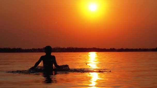 Silueta chlapce při západu slunce vyvolává ruce a vytváří vodní potřísnění. Zpomaleně — Stock video