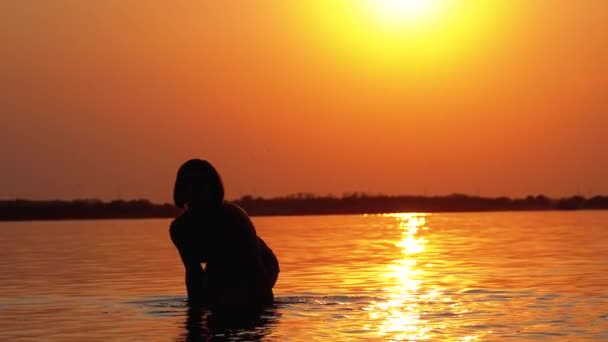 Silhouet van de vrouw bij zonsondergang verhoogt de handen en het creëren van spatten van water. Slow Motion — Stockvideo