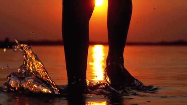 Silhouette of Legs of Boy Correndo para a água ao pôr do sol e criando respingos. Movimento lento — Vídeo de Stock