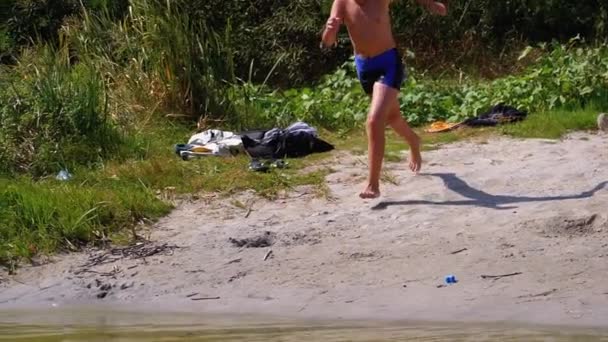 Pojke som springer in i vattnet på strand stranden och skapar stänk i floden. Slow motion — Stockvideo