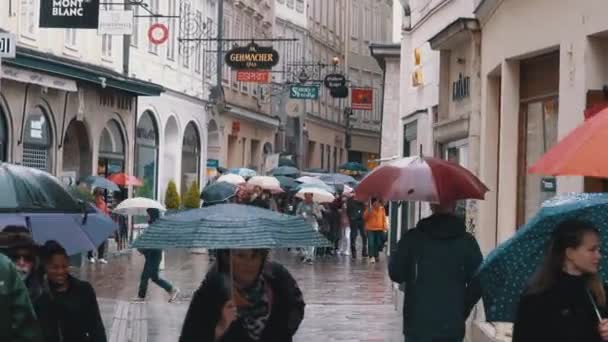 Menschen mit Regenschirmen laufen bei Regen durch die Straßen der Altstadt von Salzburg. Österreich — Stockvideo