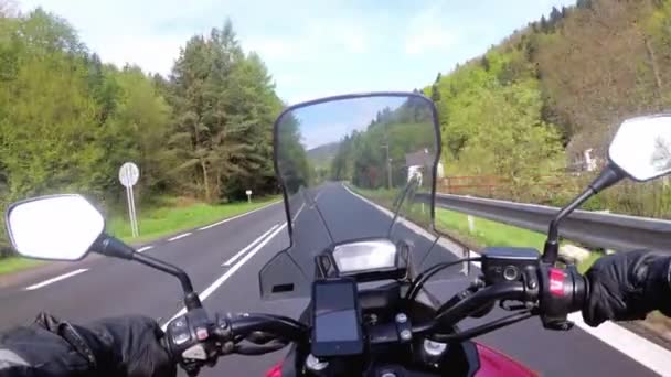 Motocyklista jazda na pięknej pustej drodze w pobliżu zielonych drzew i wzgórz — Wideo stockowe