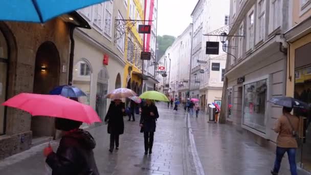 雨の中、傘を持つ人々は、旧ザルツブルクの通りを歩きます。オーストリア — ストック動画
